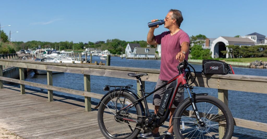 Man standing on a boardwalk in Patchogue, NY, enjoying a view while drinking next to an e-bike.